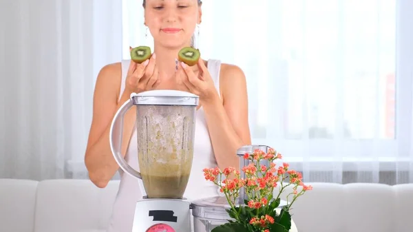 Glückliche junge Frau bereitet köstlichen nahrhaften Smoothie im Kiwi-Mixer zu — Stockfoto