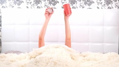 Yatakta bir fincan kahve ve çalar saati olan kadın eller, yeni bir güne başlama kavramı, günaydın. Yeni bir işe başla..