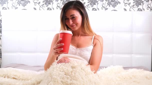 Zabawna kobieta siedząca w łóżku z kawą na wynos, ciesząca się porankiem i pijąca kawę. Koncepcja rozpoczęcia nowego dnia, relaks w weekend, nie trzeba nigdzie spieszyć, dzień dobry — Wideo stockowe