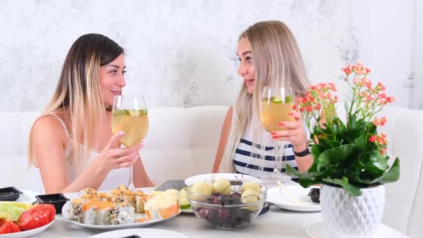 Twee aantrekkelijke meisjes, vrolijke beste vrienden die plezier hebben en thuis wijn drinken. Twee glazen witte wijn in handen. Meisjes hebben plezier samen roddelen. — Stockvideo