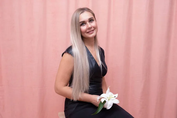 Retrato de la chica más hermosa con hermoso pelo largo liso con una flor en sus manos sobre un fondo rosa — Foto de Stock