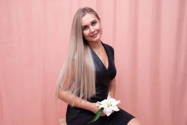 Retrato da menina mais bonita com lindo cabelo longo liso com uma flor em suas mãos em um fundo rosa — Fotografia de Stock