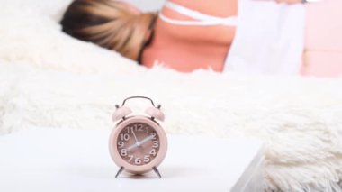 Yataktaki kadın sabah çalar saati kapatıyor. Kadın erken kalkmak istemiyormuş. Alarm saati yakın plan.