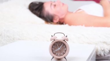 Yataktaki kadın sabah çalar saati kapatıyor. Kadın erken kalkmak istemiyormuş. Alarm saati yakın plan.