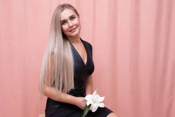 Retrato da menina mais bonita com lindo cabelo longo liso com uma flor em suas mãos em um fundo rosa — Fotografia de Stock