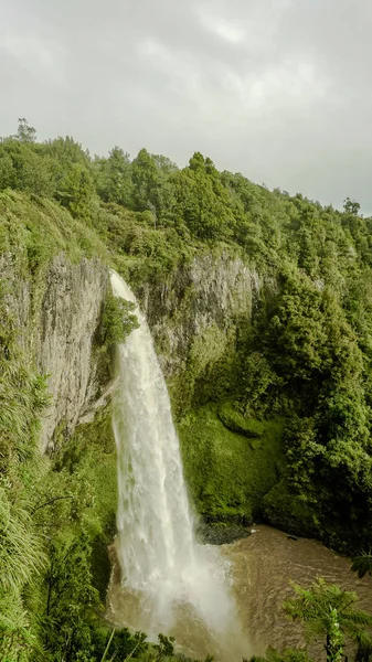 waterfall in rainforest with cloudy sky and brown water