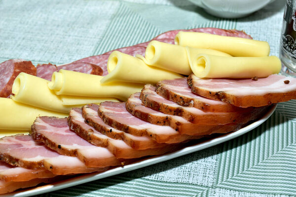 On a ceramic dish lies thinly sliced fatty smoked meat, sausage and cheese.