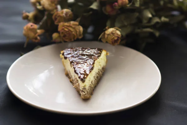 チョコレートと黒の背景の上に花のチーズケーキのスライス — ストック写真