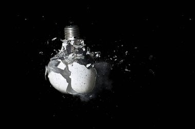 Sabit değer: cam ampul patlayan siyah arka plan üzerine beyaz. Dondurulmuş hareket. Kavramsal: elektrik fiyat artan.