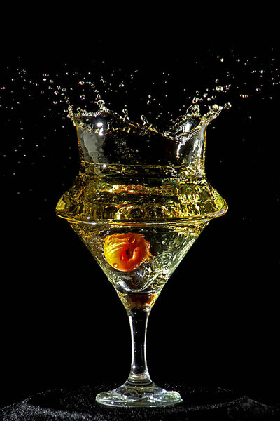 Yellow cocktail glass with an olive splashing. Black background. Frozen movement