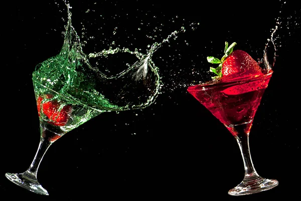 Two green and red cocktail glasses splashing. Black background. Frozen movement