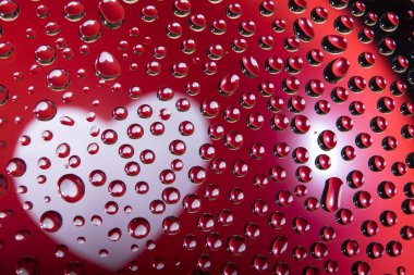 Kırmızı bir balonun üzerindeki beyaz kalp birçok su damlasına yansıyor.