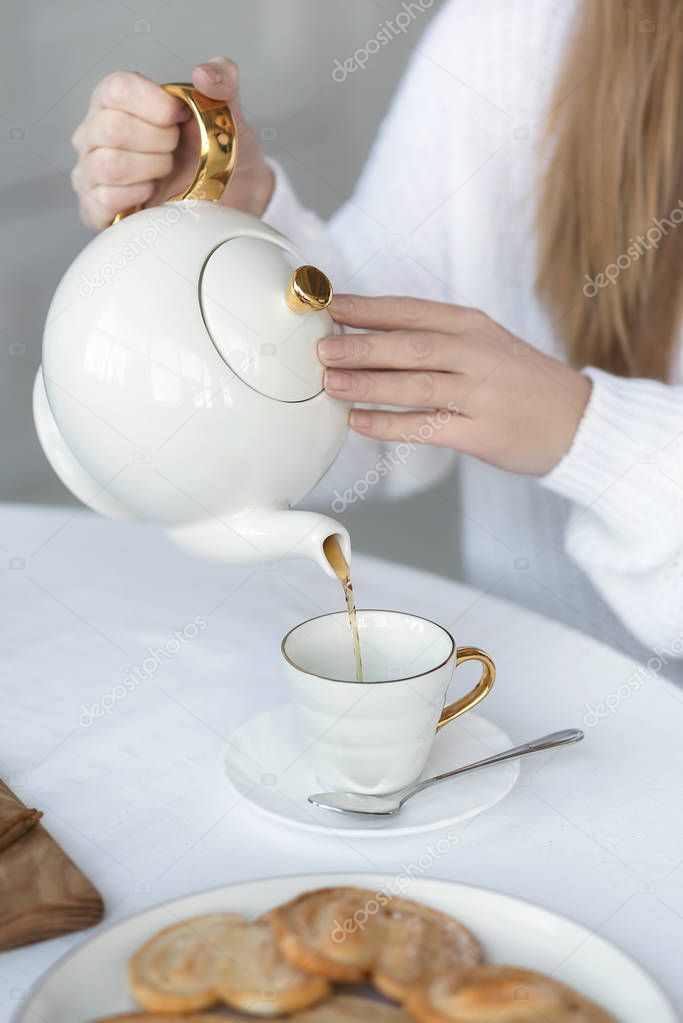 Female hands pouring tea into the cup from the kettle.