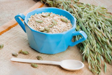 Yulaf ezmesi, kabak çekirdeği, tahta kaşık, yulaf, çul ve dokuma peçete kulakları ile mavi Kupası