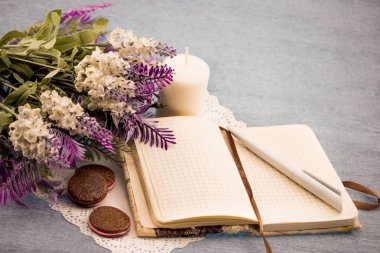 bir defter ve bir kalem, siyah bir kupa yanında beyaz peçeteye sütlü kahve vardır iki beyaz mumlar, çiçekler yalan, gri-siyah arka plan üzerinde siyah beyaz taşlar