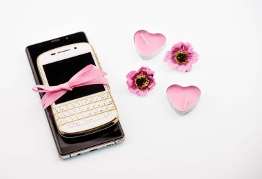 iki cep telefonu birbirinin üstüne yalan ve pembe bir kurdele ile bağlanmış. Yakınlarda gülü ve beyaz arka plan yakın çekim üzerinde iki pembe mum kalp iki çiçekler bulunmaktadır