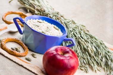 bir fincan yulaf ezmesi, bir elma, bisküvi, kumaş üzerine yulaf kulakları yanında