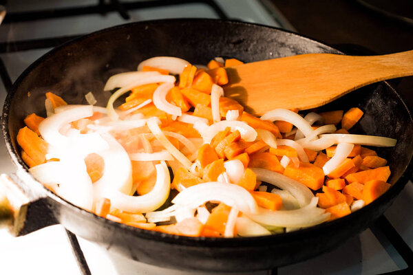 onions and carrots are fried in a heated pan