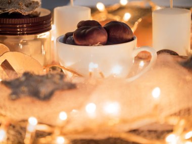 Hoş bir Noel akşamı. Bir kupa bir mum ve garland fırında kestane ile closeup