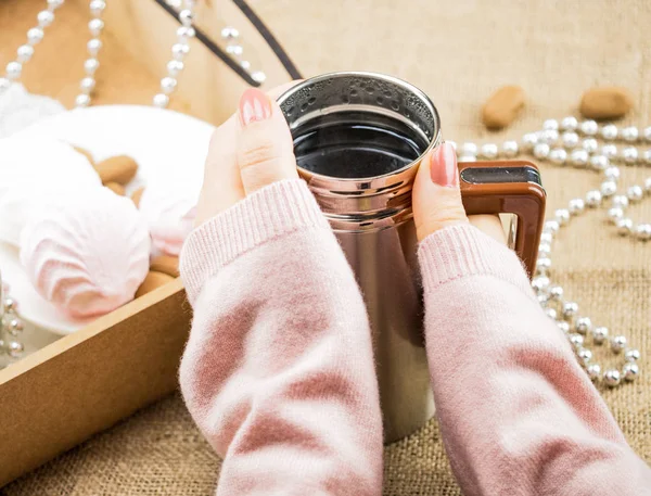 Warm the girl\'s hands on the mug, close-up. Brilliant New Year\'s beads and sweets are scattered around, a tray with sweets is close at hand. Background blurred