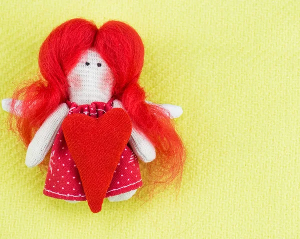 The little angel doll with a heart lies on a light green fabric. Background blurred