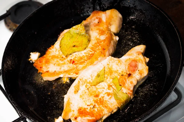 Two fried steaks are fried in a pan. The pan is on the stove. Close-up