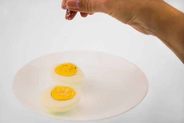 Αυγό Κομμένο Στη Μέση Ένα Λευκό Πιάτο Γυναικεία Χέρια Αλατίσματος — Φωτογραφία Αρχείου