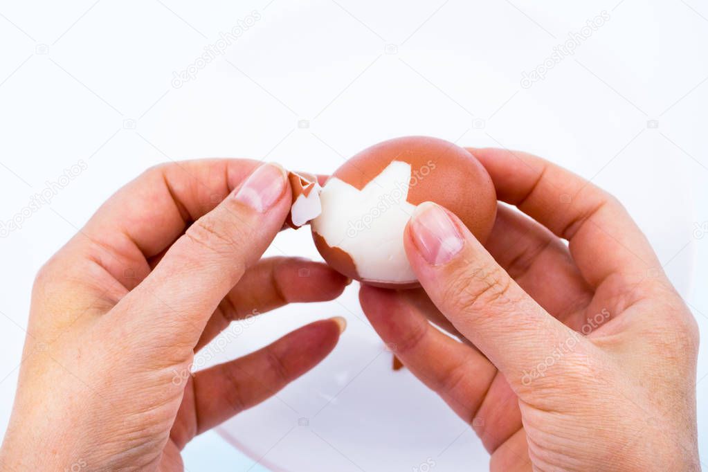 Close-up girl's hands clean chicken egg over white plate. Near the shell. Background white blurred