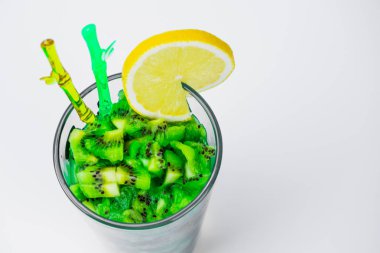 Boşaltmak. Bir bardak kivi smoothies, bir dilim limon, bir bardak tübüllerin ve kokteyl sopa içinde. Bir cam zeytin bir peçeteye duruyor. Yan görünüm, üst. Arka plan beyaz