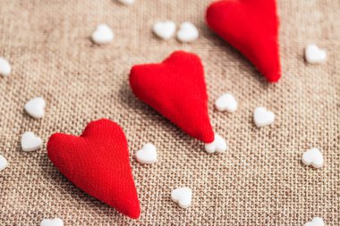 Closeup çapraz olarak üç hearts kumaştan yapılmış. Arka plan bulanık. Beyaz küçük kalpler etrafında dağınık vardır. Arka plan doğal dokuma keten, büyük