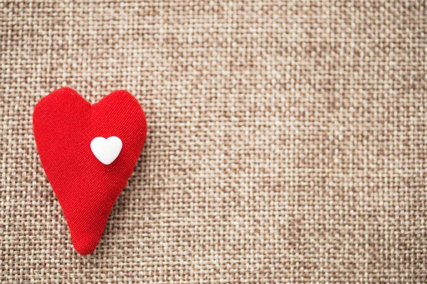 The heart of the fabric volume, red, on top is a small white plastic, to the left of the photo. Valentine\'s Day. The background is blurred. Background natural flax, large weaving. Copyspace