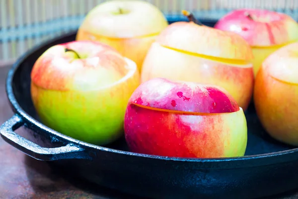 Close-up of apples in a frying pan with cut off lids. Apples are prepared for roasting in the oven. Side view. The foreground is clear, the back is blurry. In the background is a bamboo mat, blurry
