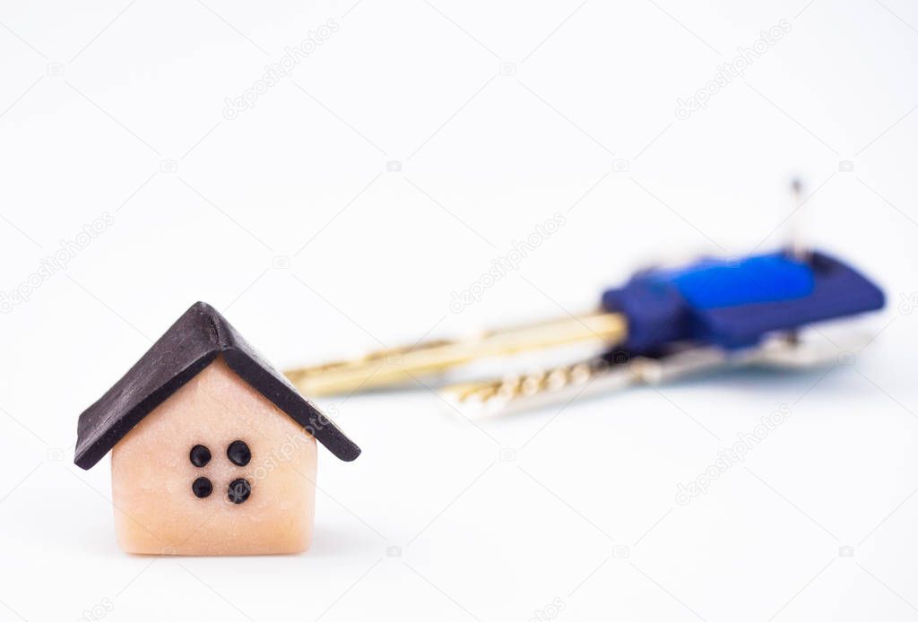 Symbol house made of plastic close up. In the background, the keys to the apartment are blurry. The background is white, blurred. There is a place to sign the copyspace.