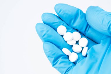 Elinde mavi Medikal eldiven kapatalım. Doktor avuç beyaz yuvarlak hapları tutar. İlaç fotoğraf sağ elinde. Beyaz arka plan, imza, boşaltmak için yer