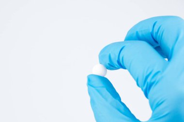 Elinde mavi kauçuk eldiven kapatalım. Doktor bir beyaz yuvarlak hap iki parmağınızla sağdaki fotoğraf tutar. Beyaz arka plan, imza, boşaltmak için yer