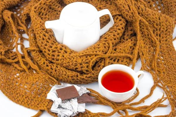 Tea in the winter evening. A cozy evening with a cup of tea and chocolate. On a white background a warm knitted scarf warms the tea. Closeup, top view side view