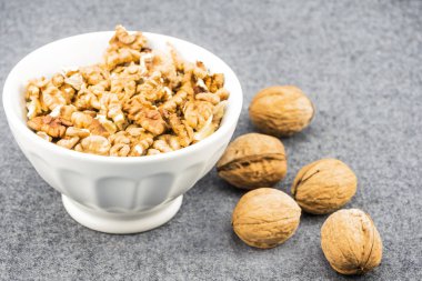 Yanındaki masaya ceviz soyulmuş ceviz çekirdek ile beyaz bir tabak bulanık, yakın çekim, en iyi görünüm, yan görünümü vardır. Arka plan gri, kumaş bulanık