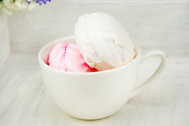 Beyaz ve pembe şekerleme, closeup ile beyaz kupa. Arka plan beyaz eski püskü, boyalı tahta, yaşlı yüzey. Sol üst köşesinde çiçek olur. Yan görünüm