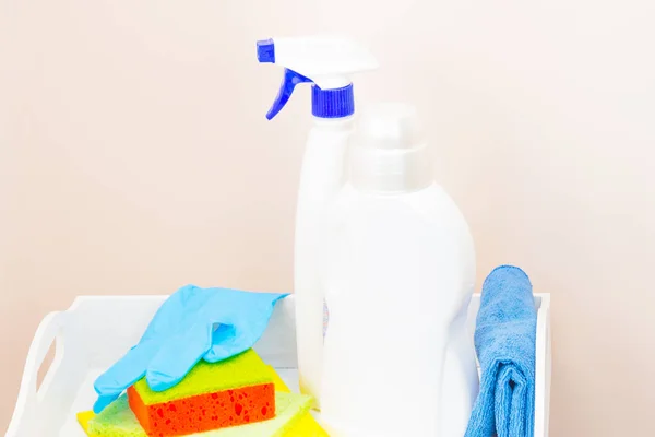 Cleaning the house using cleaning products. The concept of cleanliness and comfort. On a light pink background, a white tray, detergent, washcloths. Closeup side view