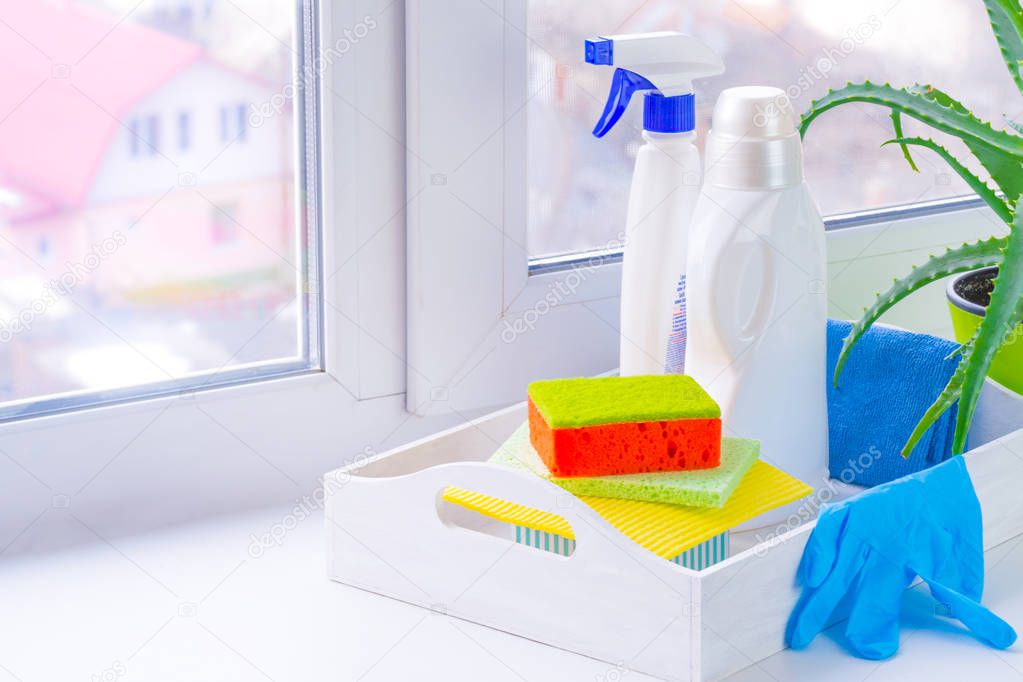 Spring cleaning. Window cleaning using bottle cleaners. On the windowsill is a white tray and detergent, washcloths. Near the pot with aloe. Outside the city, blurry