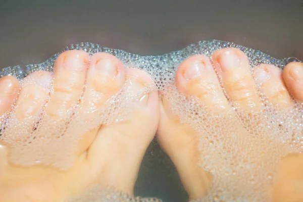 A woman washes her feet. Dirty feet in a basin of foam