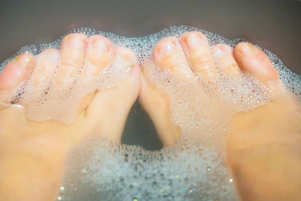 A woman washes her feet. Dirty feet in a basin of foam. Toes, close-up. Spa treatments, relax