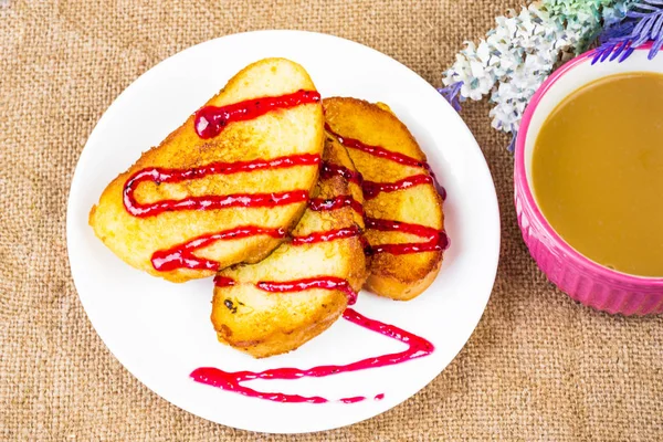 Croutons with berry topping on a white plate and a bright pink mug with cappuccino. View from above. Fruit topping on toasts. Good morning, delicious breakfast. Background rustic burlap decor of flowers