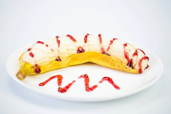 Banana with berry topping on a white plate. Background white close up