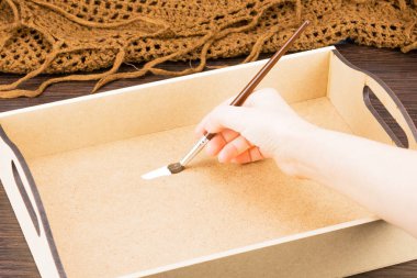 Biz eski tepsi ahşap yüzeyine süsleyin. Ahşap parçaları ile beyaz boya boyama. Kızın elini bir fırça ile sunta, kaba vuruş beyaz akrilik boya yüzeyine Dekorasyon üzerinde el ile iş yapan