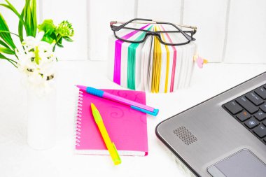 Kadınların office çalışma ortamında. Bir dizi ileti örneği, bir defter iş kadını, yazma, çıkartmalar, gözlük ve açık renkli bir dizüstü bilgisayarda bir paket beyaz çiçek bileşimi ile çok renkli kalemler. Kavram erkek