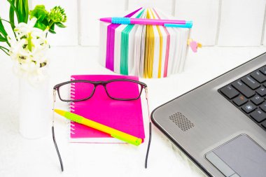 Kadınların office çalışma ortamında. Bir dizi ileti örneği, bir defter iş kadını, yazma, çıkartmalar, gözlük ve açık renkli bir dizüstü bilgisayarda bir paket beyaz çiçek bileşimi ile çok renkli kalemler. Kavram erkek