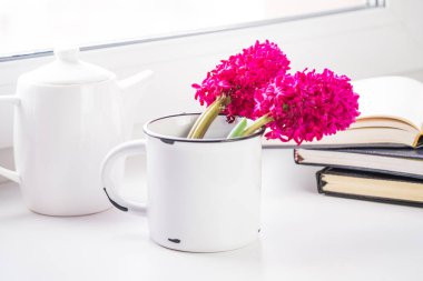 Beyaz çay Servisi, pencere pervazı pembe sümbül çiçekleri ile büyük bir metal beyaz kupa yanında. Arka planda birkaç dizüstü bilgisayarlar, bir açıktır. Günaydın ve bahar kavramı