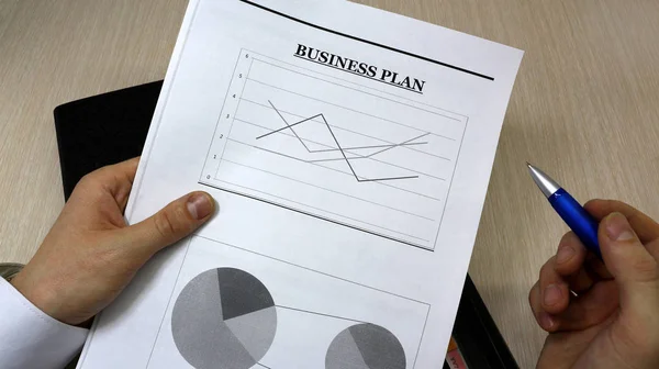 Job with finances in the office on a laptop,the employee holds paper with the inscription business plan.Businessman analyzes the chart of the rise or fall of prices and is a plan of action. marketing course in business