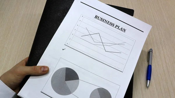 Job with finances in the office on a laptop,the employee holds paper with the inscription business plan.Businessman analyzes the chart of the rise or fall of prices and is a plan of action. new business idea